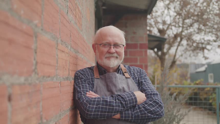 Bearded man wearing an apron reclined on the brick wall of a house on the backyard