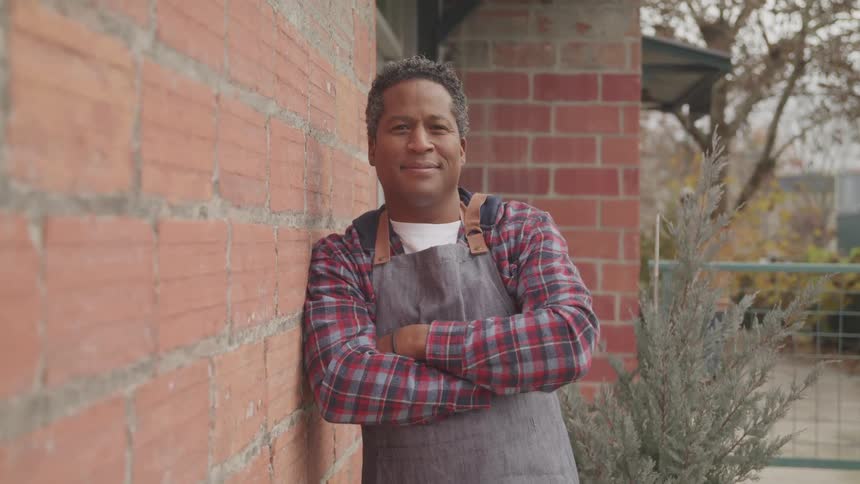 Man wearing an apron reclined on the brick wall on the backyard