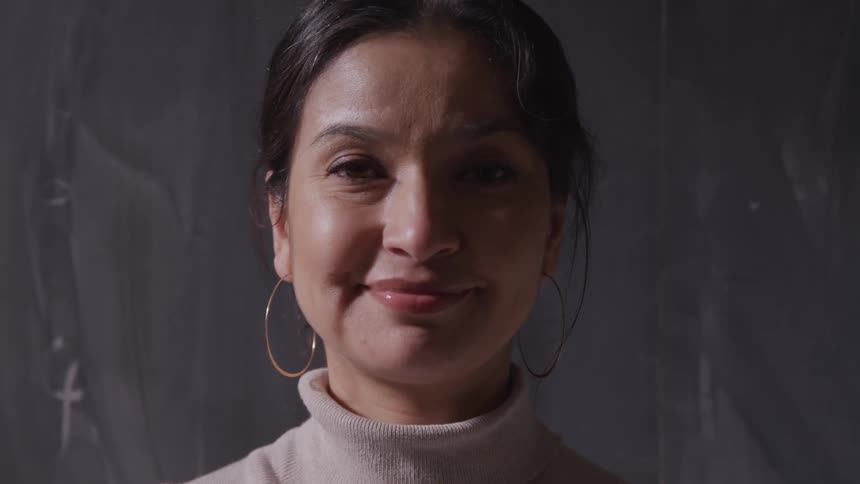 Woman with hoop earrings and a grey turtleneck sweater smiles slightly and looks at the camera