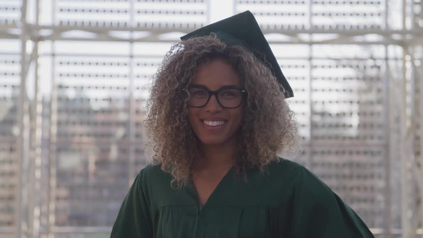 A young woman smiles in her cap and gown for graduation