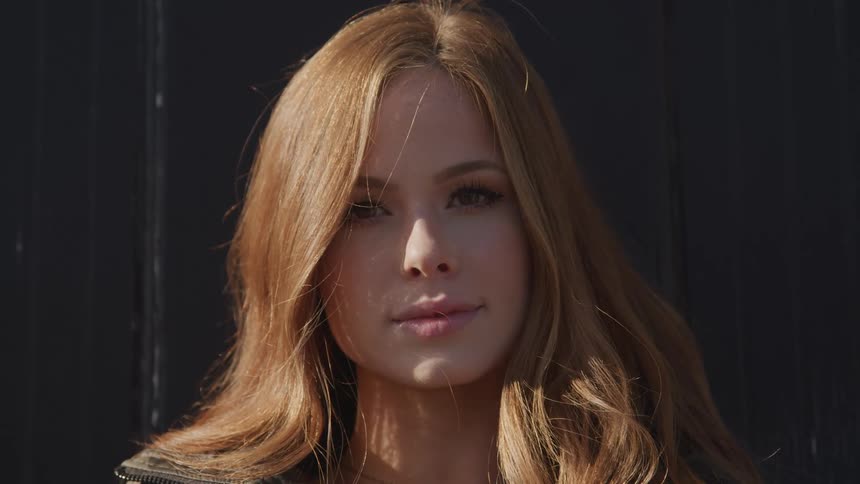 Woman with red long hair and makeup faces the camera with eye contact