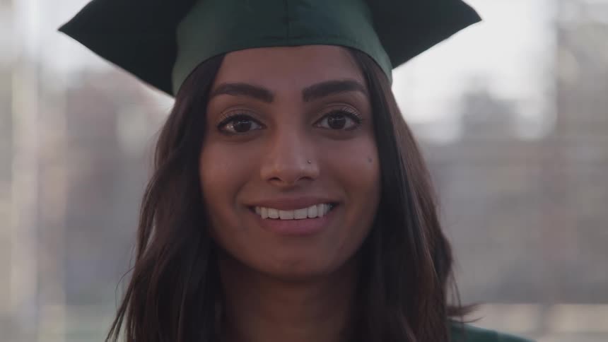 Woman in graduation cap and gown turns her head and smiles