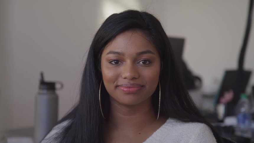 Woman with a white sweater and big hoop earrings smiles and looks at the camera in an office