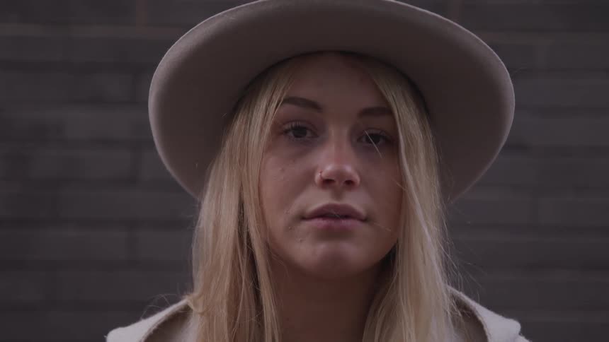 A young blonde haired woman wearing a hat looks forward into the camera