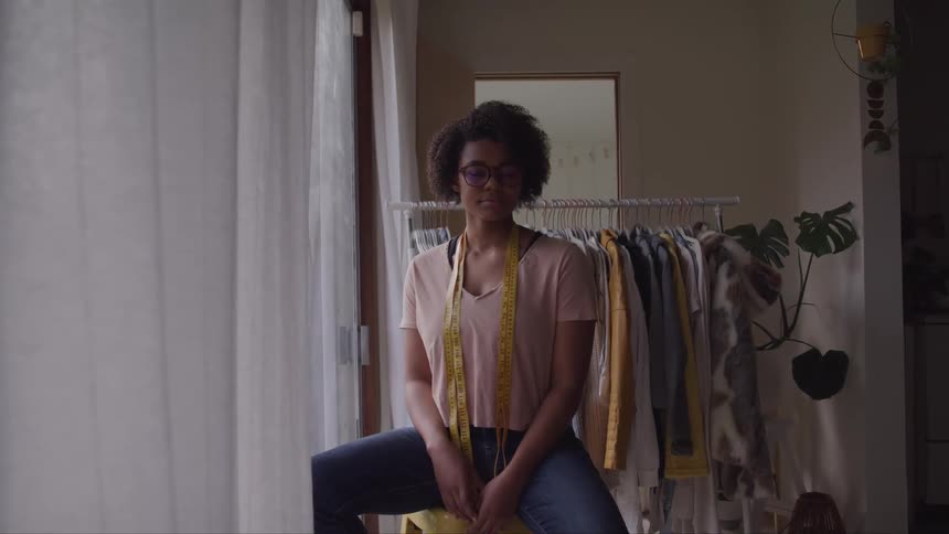 A fashion designer poses with a measuring tape around her neck in front of a clothing rack