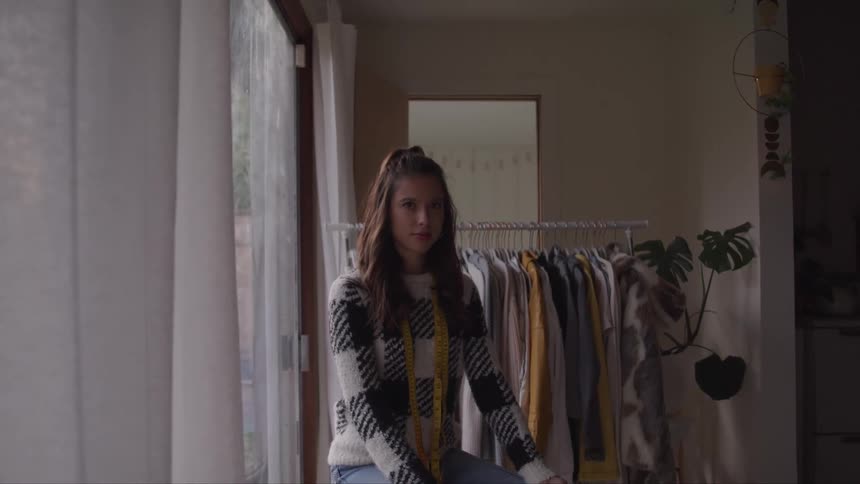 Young woman wearing a sweater sitting in a room at home looks at the camera