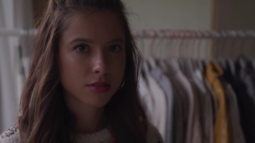 A woman is standing in a closet next to clothes