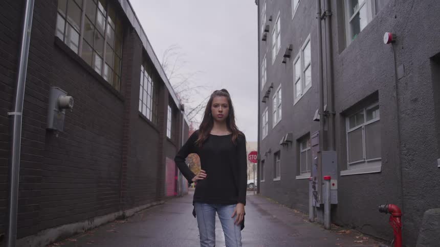 Woman brown hair a black sweatshirt and jeans stands her hand on her hip in a narrow street between two buildings