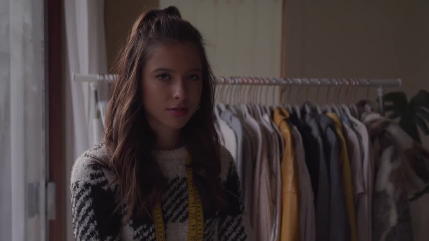 A teenage girl working in a clothing store stands with a tape measure around her neck