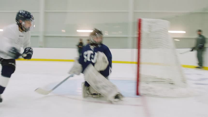 A hockey player skates and shoots the puck towards a net with a goalie in it