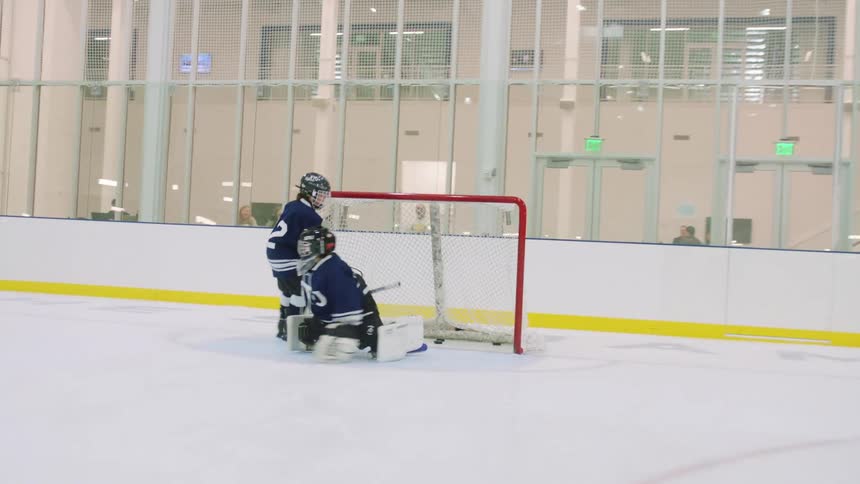A group of kids play hockey on an indoor rink as parents watch
