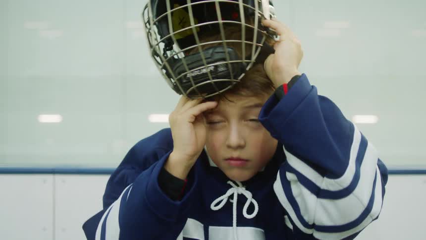 A young boy puts on his hockey mask while standing just outside the ice rink