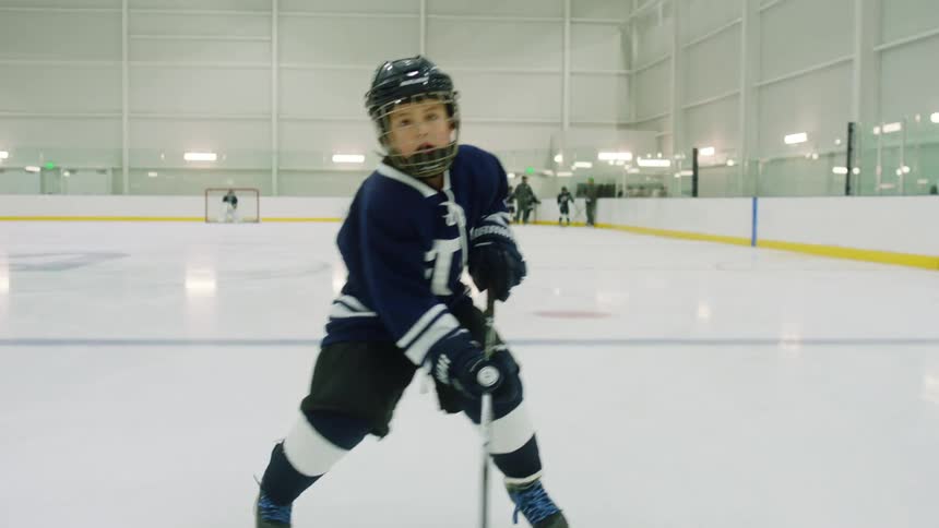 A boy in a full hockey uniform skates down the rink and moves a hockey puck to the other side