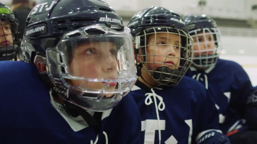 A childrens hockey team kneel as they wait in their hockey equipment on a hockey rink