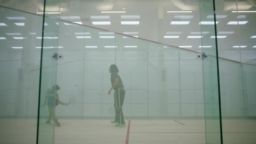 A man and woman play racquetball together on a closed off indoor court