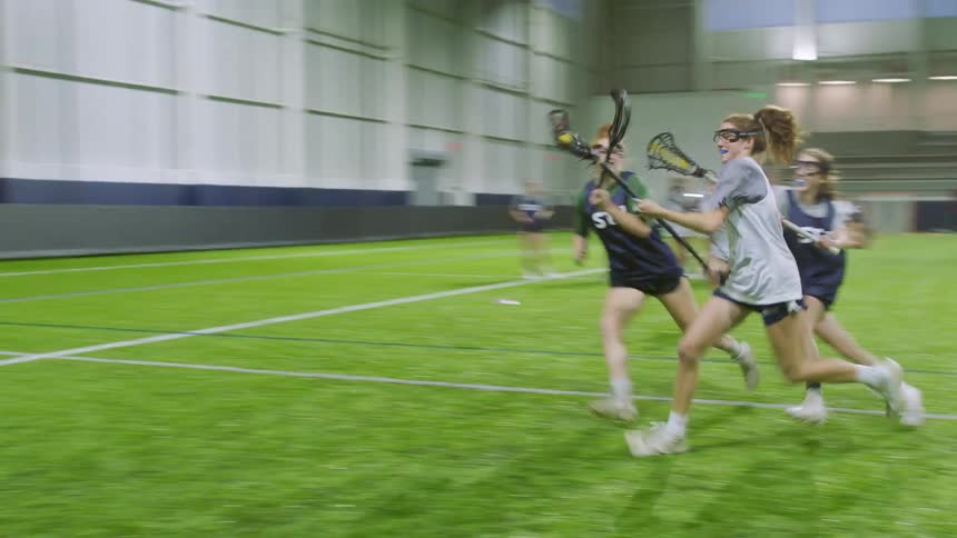 Teenage girls playing lacrosse in an indoor arena