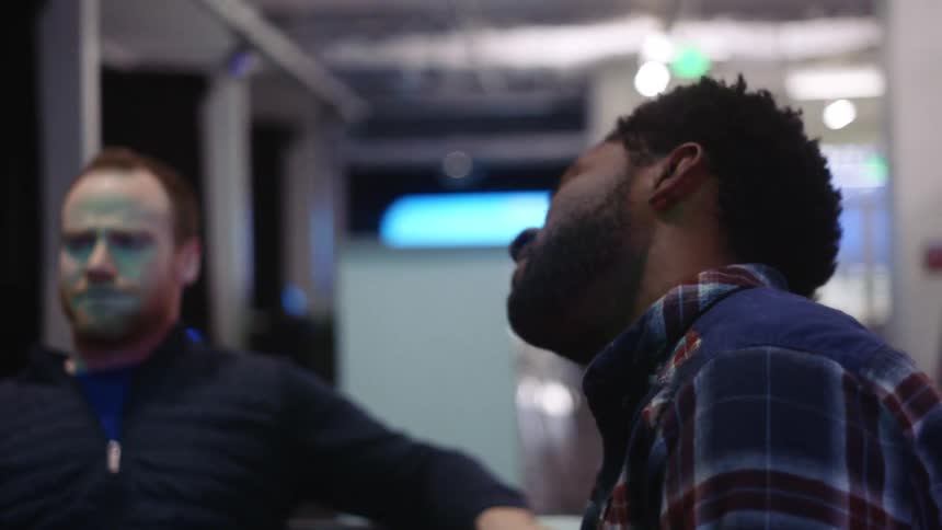 Two men sitting and talking with lights and windows in the background