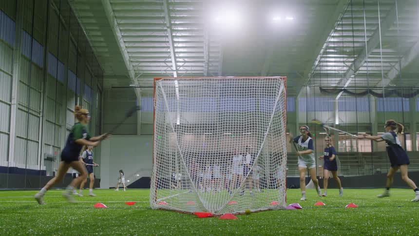 Teenage girls playing lacrosse at an indoor arena