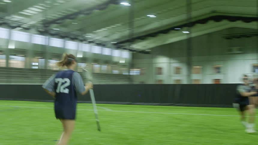 Female lacrosse players practice by running and passing a ball to each other using their sticks