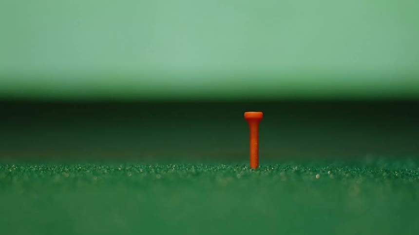 Golf ball on a red tee over green artificial grass hit by a golf iron