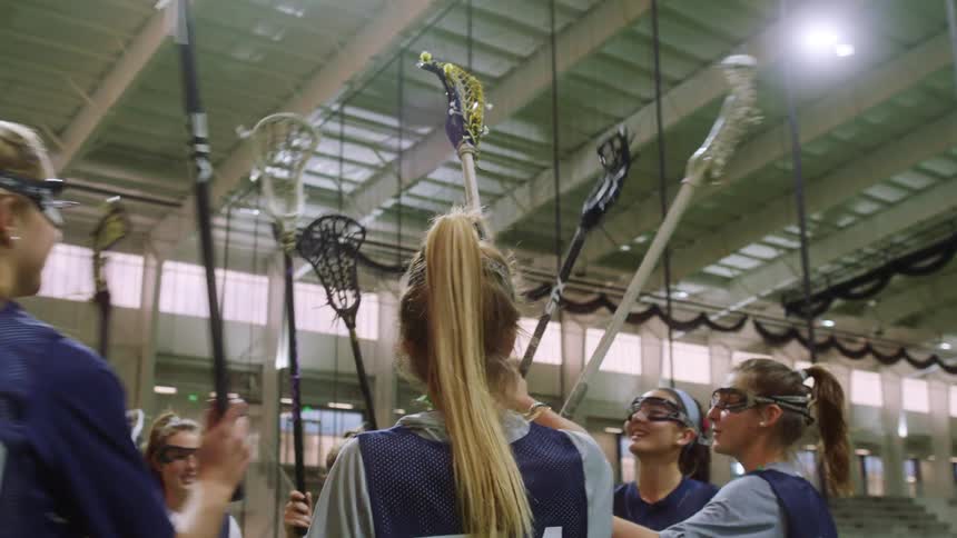 Female lacrosse players raise their sticks together in gym