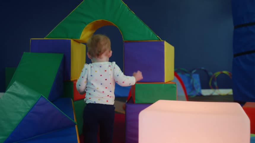 A young toddler walks through a playspace with foam blocks