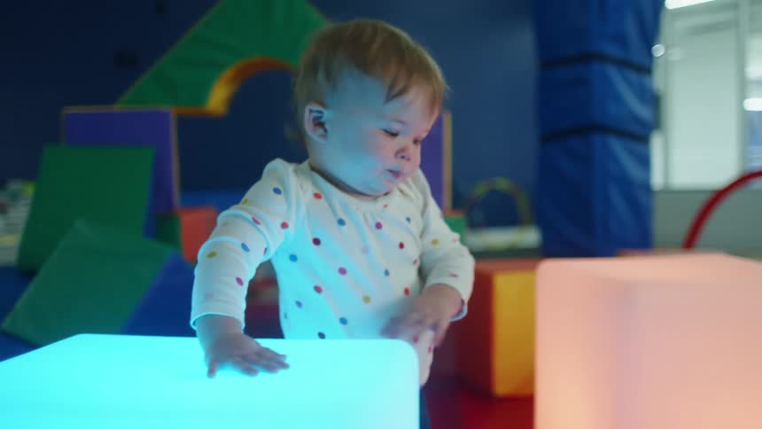 A toddler examines large glowing blocks in a playroom in an office building
