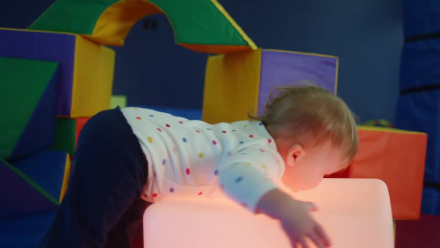 Toddler playing with a cube emitting a soft pink light in an indoors playground