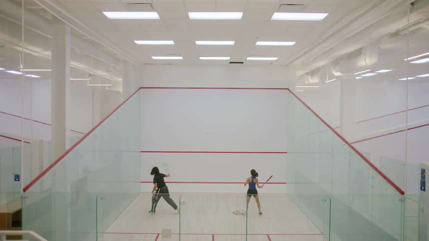 A man and a woman playing squash in a court with lights above