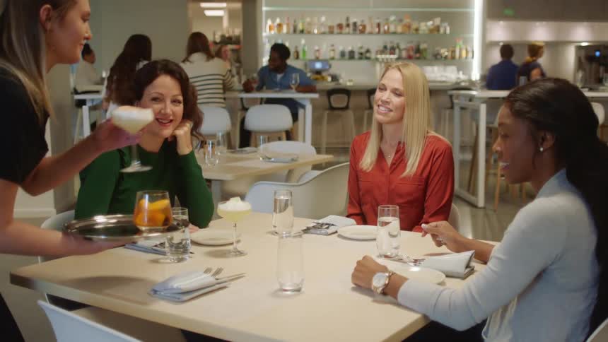A waitress serves alcoholic drinks to three women sitting at a table in a restaurant