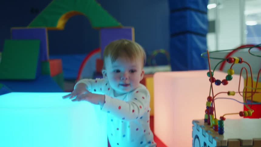 A young toddler walks in a playroom with building blocks and toys