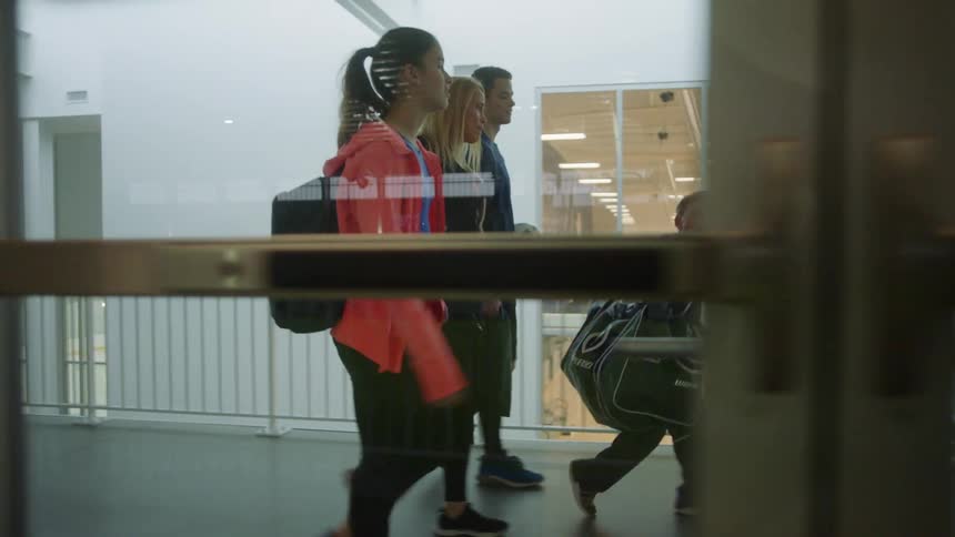 A mother and her children walk through a building with hockey equipment and a soccer ball