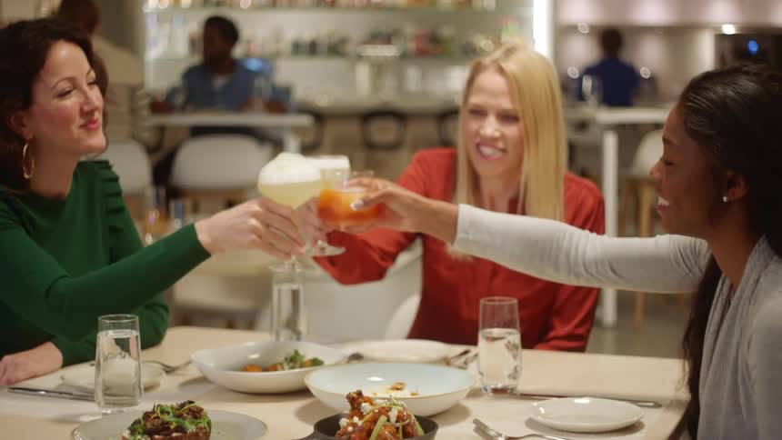 A group of women in a restaurant raise their glasses together to toast