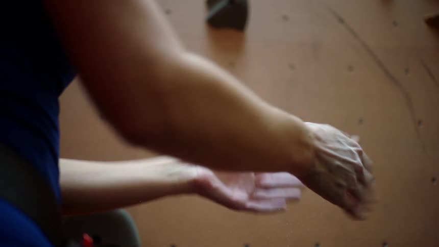A woman rubs chalk on the palms of her hands prior to starting to climb on the nearby climbing wall