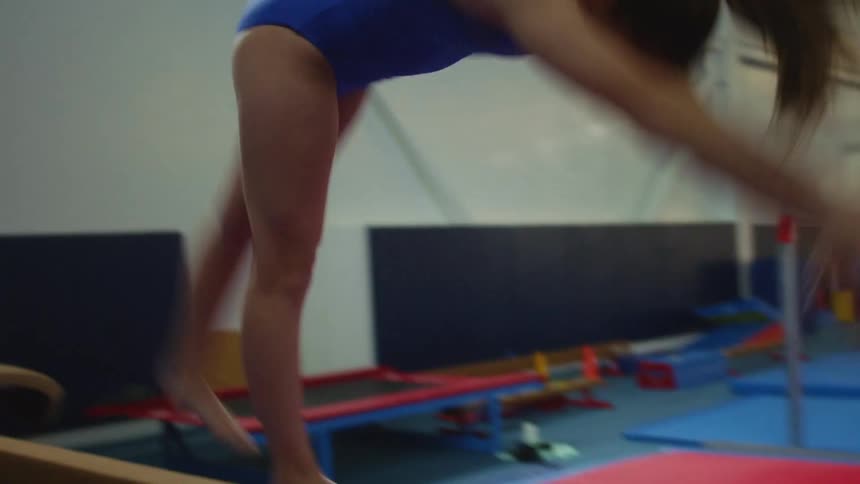A teenage girl does a back flip on a gym balance beam