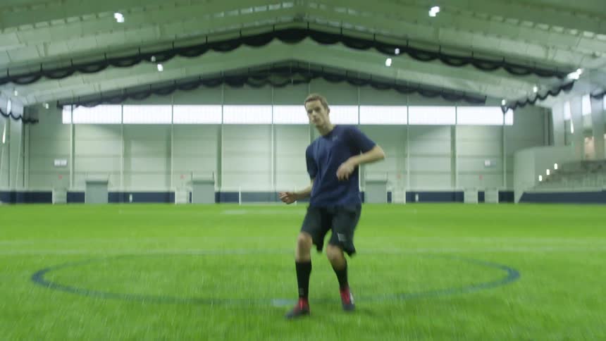 A male soccer player runs up and kicks the ball in an indoor stadium