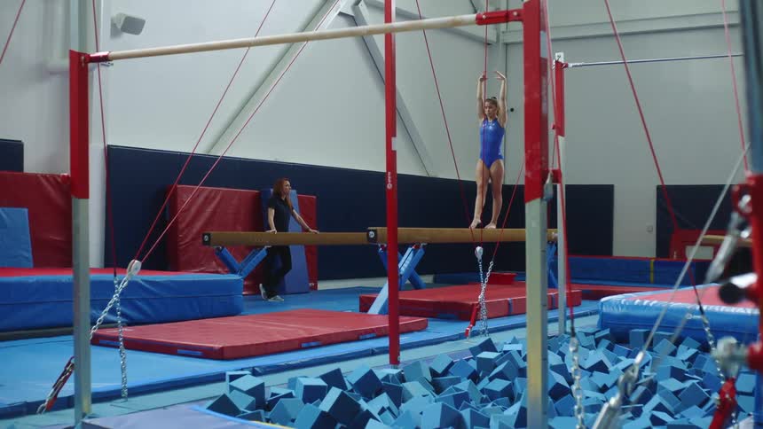 A young female gymnast practices a routine on a balance beam before dismounting into a somersault