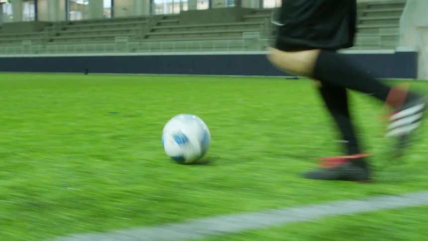 A person in an indoor football field running and kicking a football