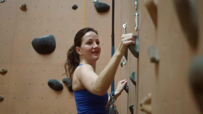 A woman carefully ascends an indoor rock climbing wall