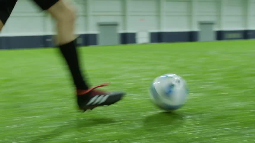 A soccer player runs and kicks the ball in an indoor arena