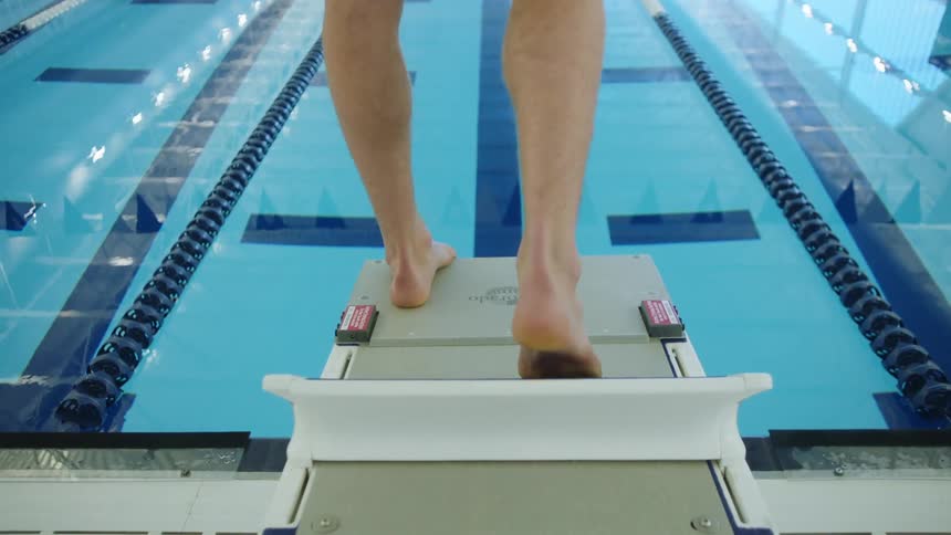Man standing on a springboard of an olympic pool gets ready to jump