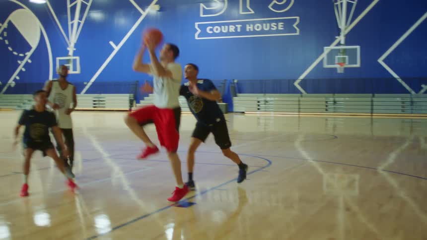 A teenager throws a layup during a two by two game of basketball in a gym