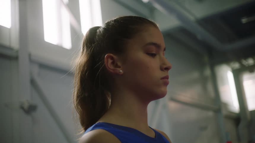 A woman with earrings standing in a gym with windows in the background