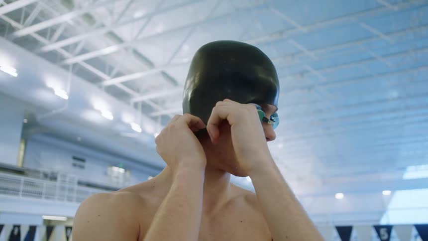 A teenage boy with swim goggles on adjusts his swim cap