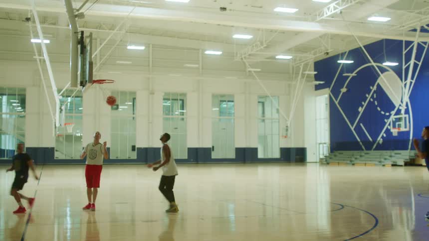 Four teenage boys playing basketball in a gymnasium and one boy shoots and makes the basket