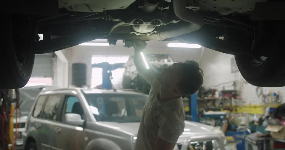 A mechanic uses a light to look underneath a car
