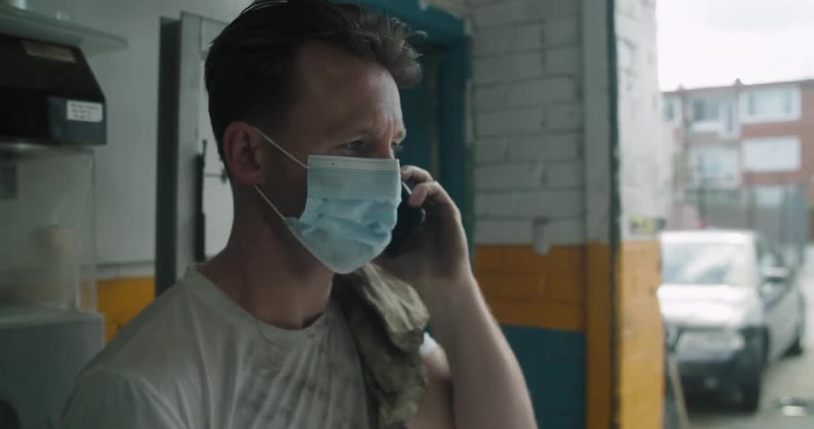 Man with a mask and a dirty white t shirt talks on a smartphone