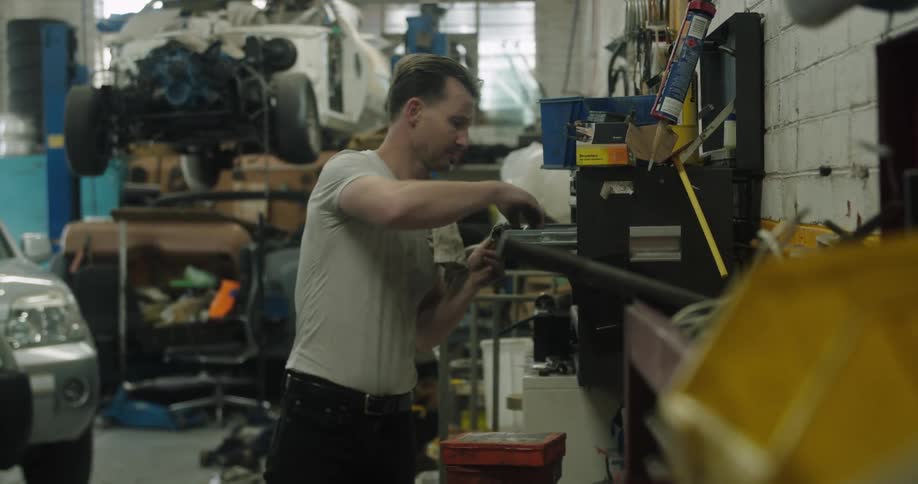 A mechanic walks over to his tool box and takes something out