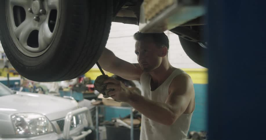 A mechanic tightens a bolt on a tire as he stands underneath a car