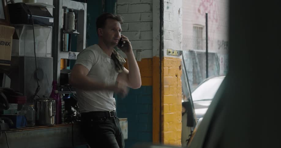Car mechanic with a dirt t shirt and jeans talks on the smartphone in the garage